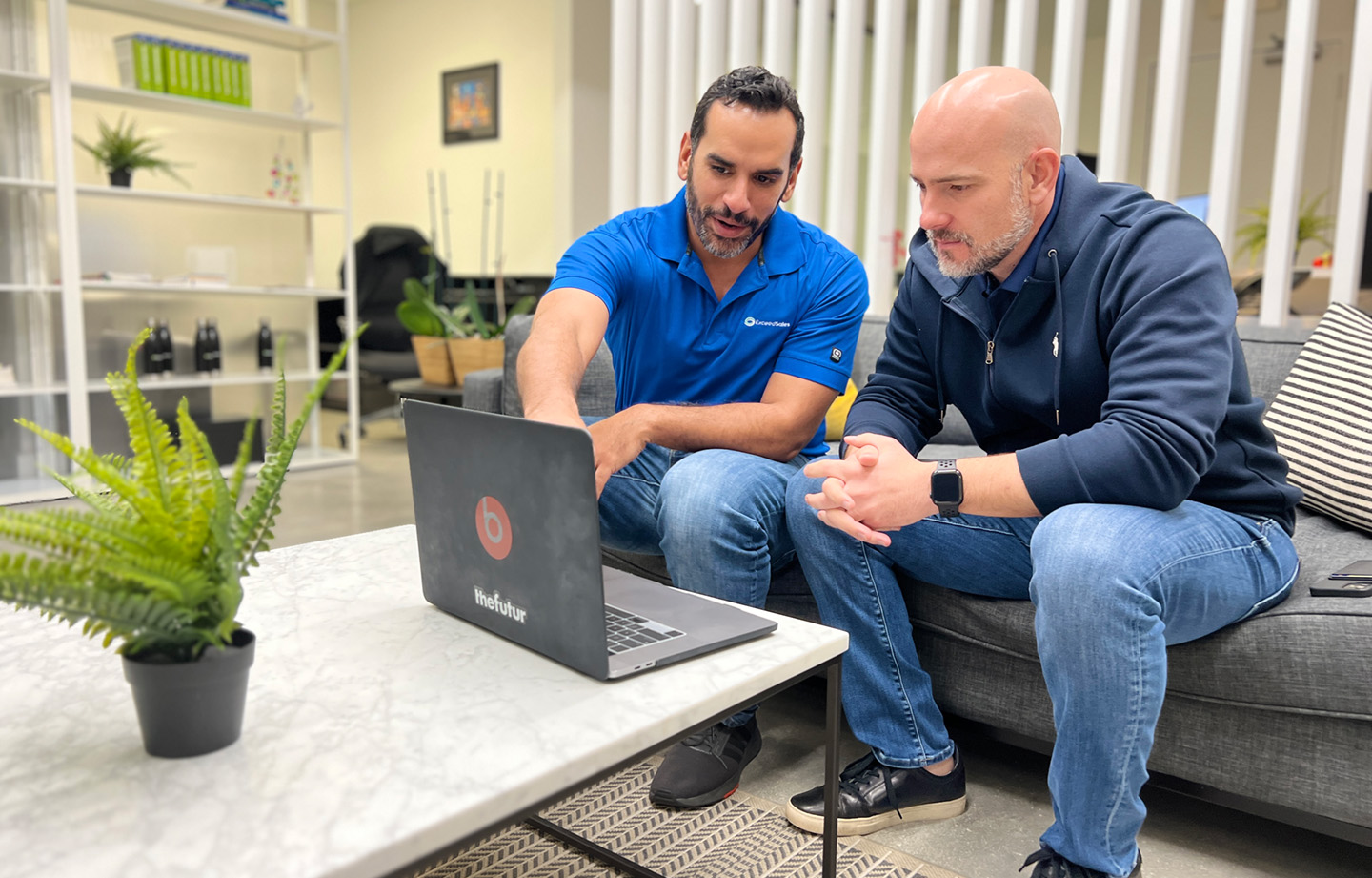 A sales coach teaches an accountant on a laptop in an office